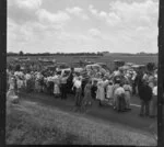 Royal tour procession, with people waving as the royal car goes past and aircrafts on display in a field behind, Rukuhia, Waikato