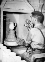 Unidentified man glazing a Temuka pottery jug before returning it to the kiln