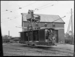 Men in a Christchurch Tramways vehicle, repairing tram wires, tram shed in background