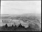 View over Dunedin, showing Otago Harbour, and construction of buildings for New Zealand and South Seas International Exhibition at Logan Park