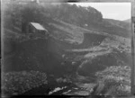 Otira Gorge, Westland District, featuring men digging and working on the entrance for the Otira Tunnel, with tent dwellings on the hillside