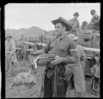 Rider Jim Ham carrying his saddle, Raetihi rodeo