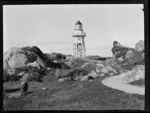 Unidentified lighthouse with surrounding large rocks and dog, [West Coast Region]