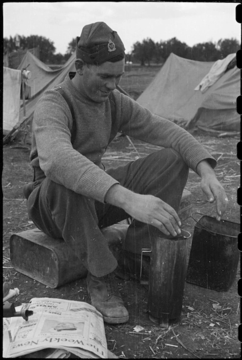 Image: Private A J Leakey warms his hands over a Benghazi Burner at the NZ LOB Camp near Capua, Italy, World War II - Photograph taken by George Bull