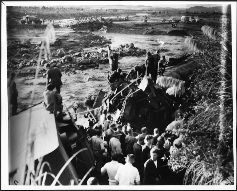 Image: At the scene of the railway disaster at Tangiwai, with a group alongside wrecked railway carriages