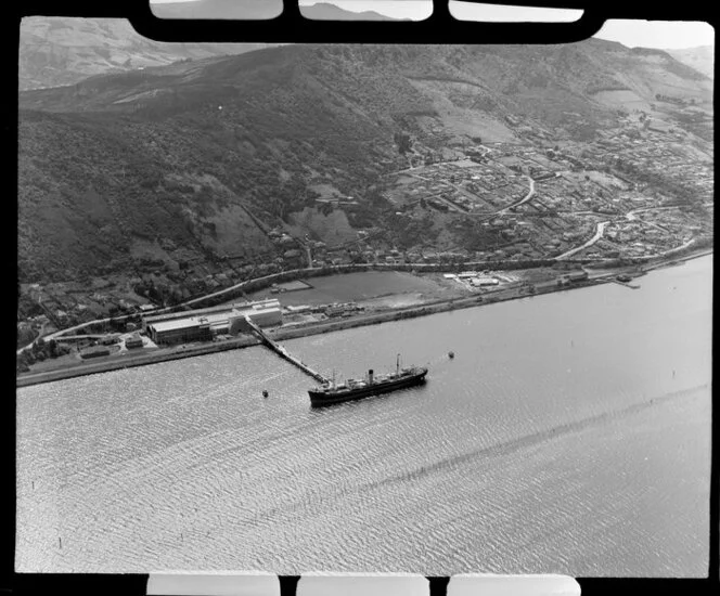 View of Ravensbourne, inner Dunedin Harbour, showing residential housing with Signal Hill above, Moller Park beside Ravenbourne Road (State Highway 88) and Ravensdown Fertiliser Works with wharf and ship