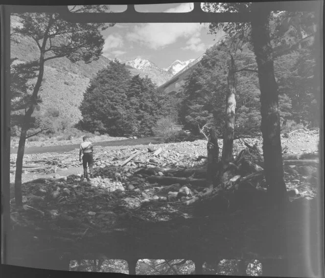 Lake Ohau, Central Otago, view of upper Temple Valley with rock covered riverbed, with man walking over to river with fishing rod, looking up tree covered valley with snow covered mountains beyond