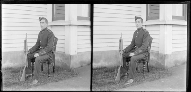 Edgar Richard Williams in military uniform seated outside house and holding a rifle, Dunedin, Otago Region