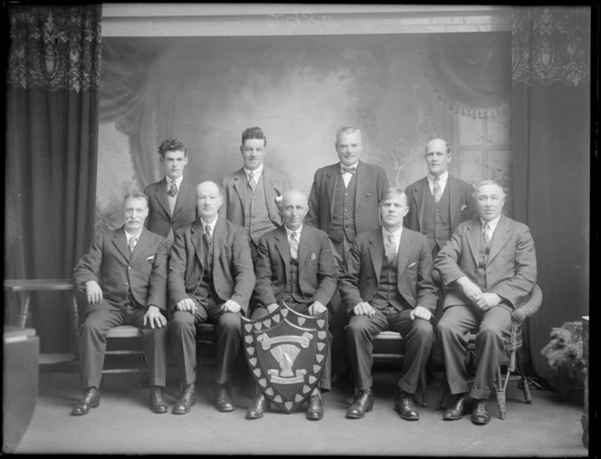 Studio portrait of nine unidentified men, winners of Christchurch United Friendly Society Annual Card Tournament shield, probably Christchurch district