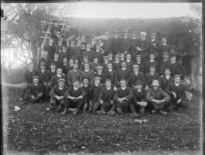 A group of unidentified men, in front of a delapidated house, possibly Christchurch district