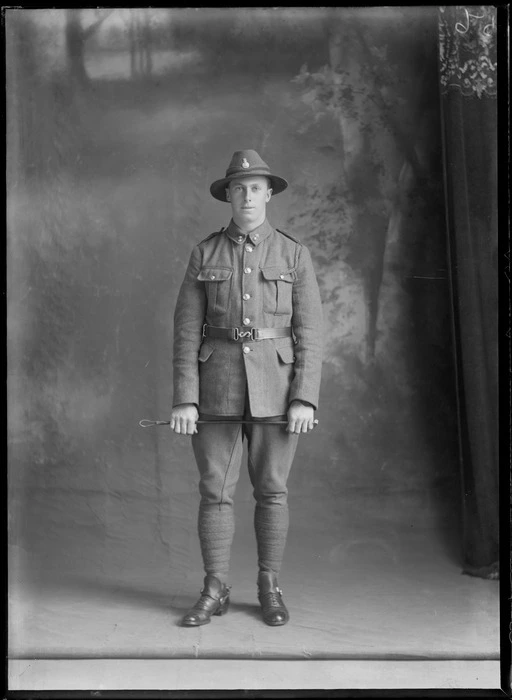 Studio portrait of unidentified young World War One soldier with hat and collar badges, standing with stirrups and riding crop, Christchurch