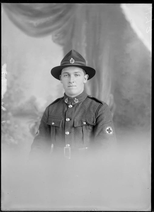 Studio upper torso portrait of an unidentified man dressed in a Medical Corps army uniform, showing the Red Cross badge on his left upper arm, with two badges on the lapels of his jacket, with a pin on his hat, possibly Christchurch district