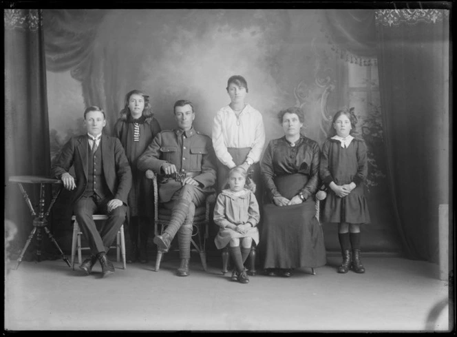 Studio unidentified family portrait, World War I soldier with star collar badges [Army Service Corps?] and wife with portrait brooch sitting with adult son and four daughters, Christchurch