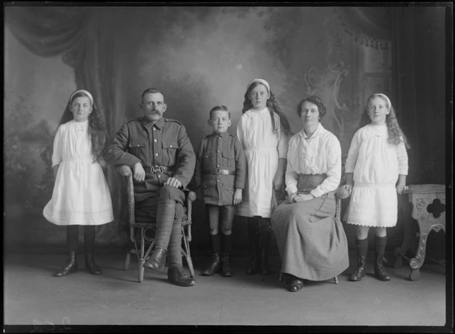 Studio unidentified family portrait, World War I soldier with large moustache and collar badges, with wife, three young daughters and young son in soldier's jacket and shorts, Christchurch