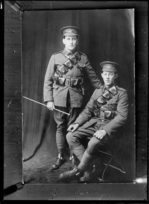 Studio unidentified portrait of two World War I soldiers with bandolier shoulder and waist ammunition belts, hats and stirrups [Mounted Rifles?], older man standing with swagger stick, location unknown