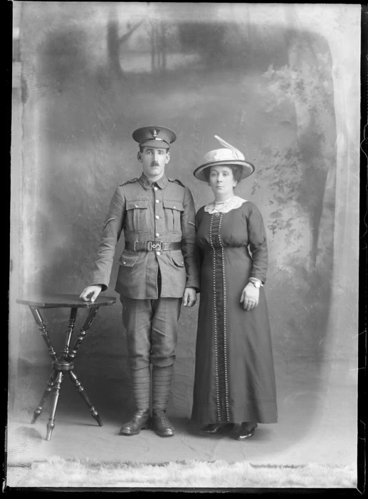 Studio portrait of an unidentified man and woman, showing man dressed in a military uniform, and the woman wearing a dress with a lace collar and a hat, possibly Christchurch district