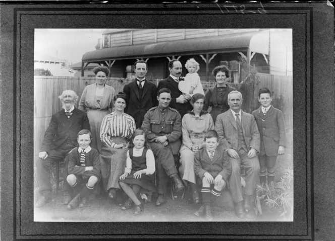 Outdoors portrait of unidentified family group taken in backyard, includes man in World War I soldier's uniform, probably Christchurch region