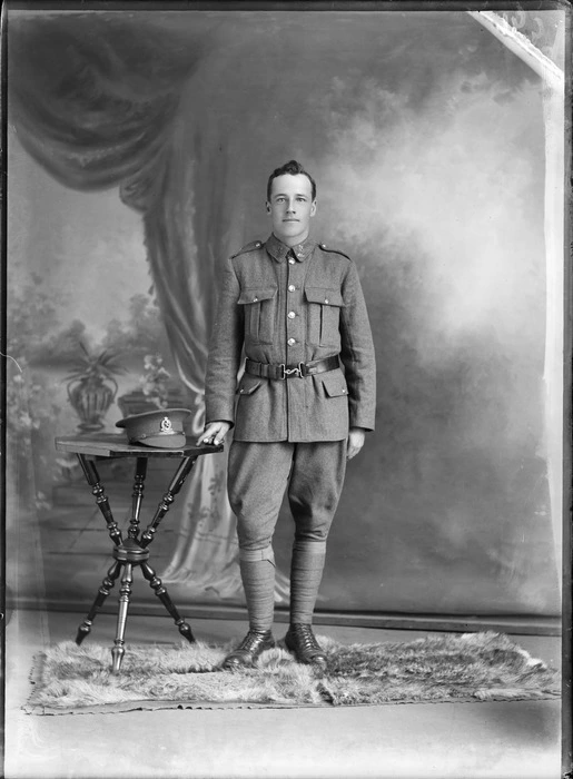 Studio portrait of unidentified World War I soldier standing with his hat on a table, with 'Liverpool' collar and hat badges [Rifle Brigade Reinforcements?], Christchurch