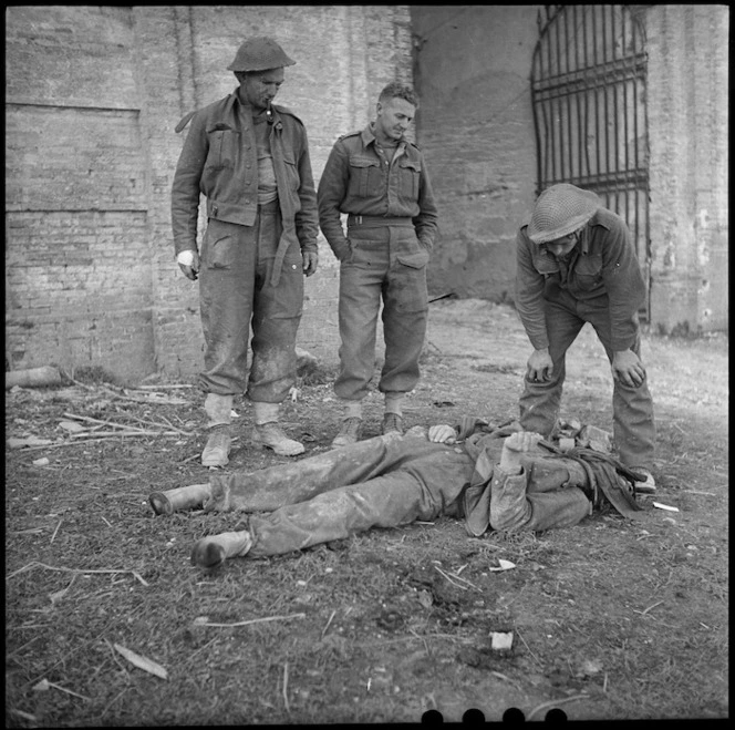 Three NZ Infantrymen survey a dead German soldier north of the Sangro River in Italy, World War II - Photograph taken by George Kaye