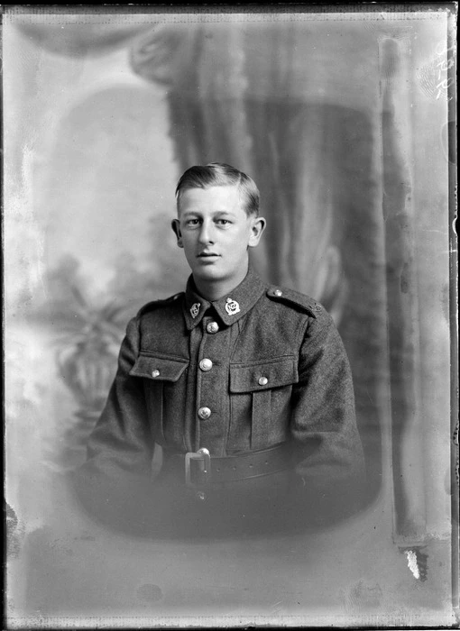Head and shoulders studio portrait of unidentified young soldier, in uniform, with two New Zealand Army badges, on his collar, featuring the letters 'NZ' between fern leaves and topped by the British Crown, probably Christchurch district