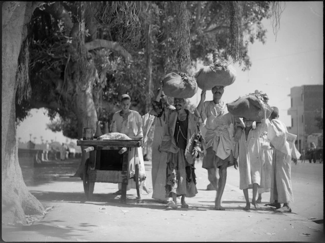 Street scene in Cairo showing local people carrying large bundles on their heads - Photograph taken by George Kaye
