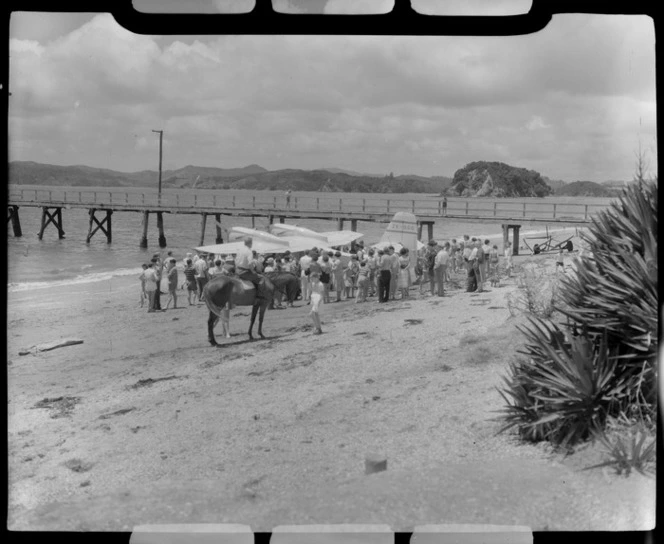 Tourist Air Travel, Grumman Widgeon aircraft ZK-BGQ at Paihia, Northland, includes crowd and a man on a horse