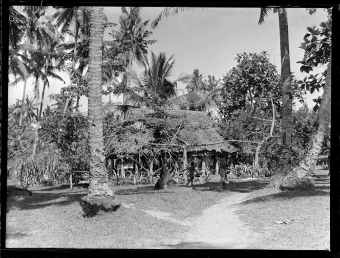 View of a native thatch roofed hut amongst palm trees with children waking by, Apia, Western Samoa