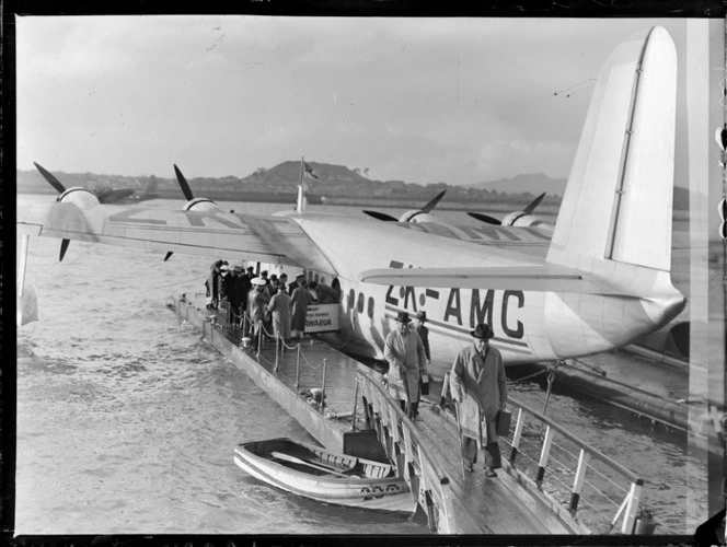 The arrival of N S Falla, the (late) Chairman of USS Co & Union Airways, off the Flying Boat ZK-AMC Awarua with unidentified crew and passengers, Auckland Harbour