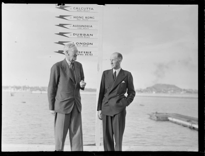 Portrait of (L to R) Sir Arch Jamieson and Colonel C W Salmon standing in front of TEAL sign post, Mechanics Bay Wharf, Auckland Harbour