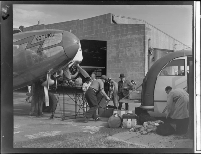 Men unloading luggage from Lockheed Electra aeroplane 'Kotuku', on to a bus, outside Union Airways hangar, Mangere, Auckland