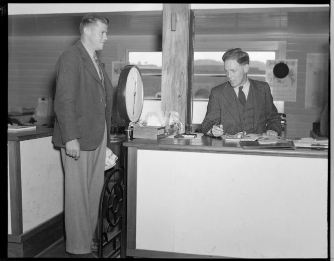 Unidentified NZNAC (New Zealand National Airways Corporation) booking agent, weighing in an unidentified passenger at a Wellington Office