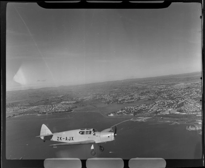 Auckland Aero Club's DH94 Moth Minor KZ-AJX plane in flight over Auckland Harbour with Hobson Bay and waterfront in view, Auckland City