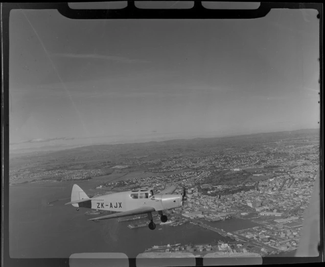 Auckland Aero Club's DH94 Moth Minor KZ-AJX plane in flight over Auckland Harbour with Auckland City and waterfront in view