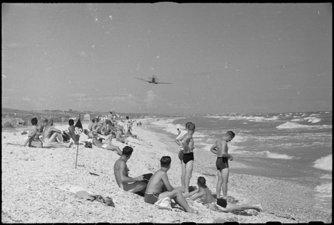 New Zealanders from Rest Camp near Ancona, Italy, watch Allied aeroplane flying over beach on Adriatic Sea, World War II - Photograph taken by George Kaye