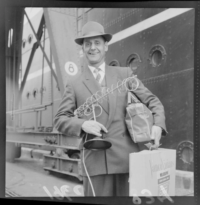 Mr A S Goldsmith, with a television antenna and Vance Vivian bags, on an unidentified Wellington wharf