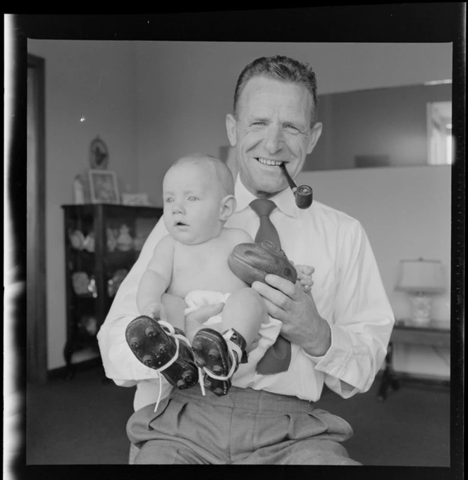 Neill McGregor holding miniature rugby ball and his baby grandson, Neill Thomas McGregor wearing small sized rugby boots