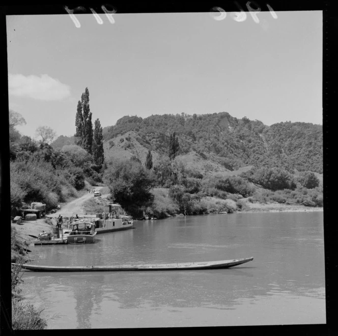 Two launches and a wooden canoe at a road end with men unloading wool bails, Whanganui River