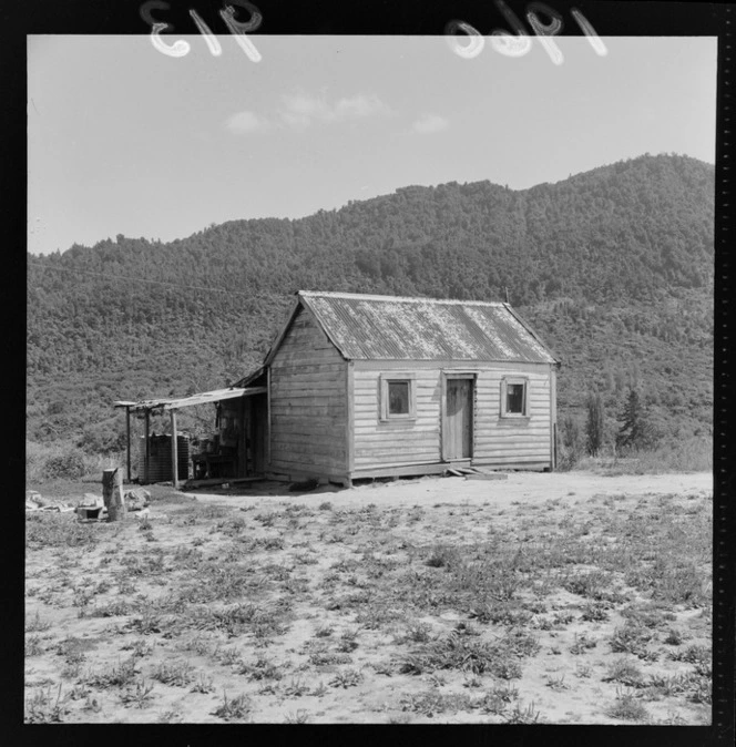 View of a whare at Pipiriki with a small single store wooden building on cleared land with forest covered hills beyond, Manawatu-Whanganui Region