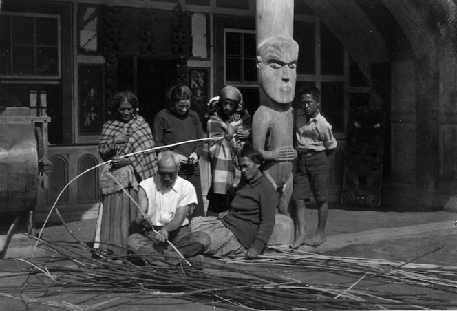 Man splitting rods of vine watched by women and a boy