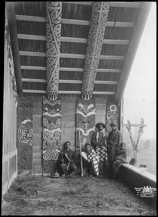 New Zealand Government Tourist Department :Photograph of group on porch of Te Whai-a-te-Motu wharenui (meeting house), Ruatahuna