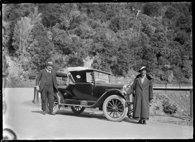 A chevrolet motor car parked at Elbow Bend on the Mount Cargill to Waitati road, with a man and woman standing beside.