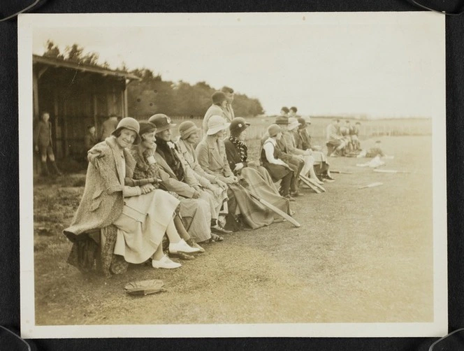 Agnes Isobel Stout and other spectators seated on the edge of a cricket field