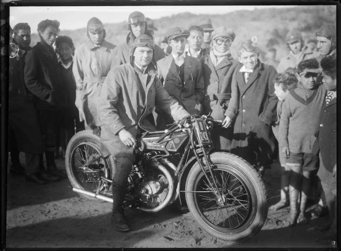 Group standing around rider on Rudge motorcycle, Otaki