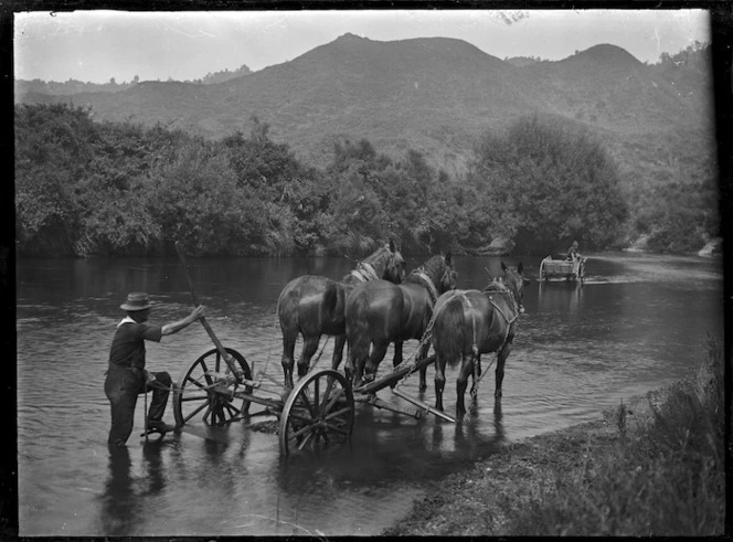 A man fording a river with a three-horse team pulling a plough-like implement, going towards another man in a dray which appears to be stuck in the middle of the river