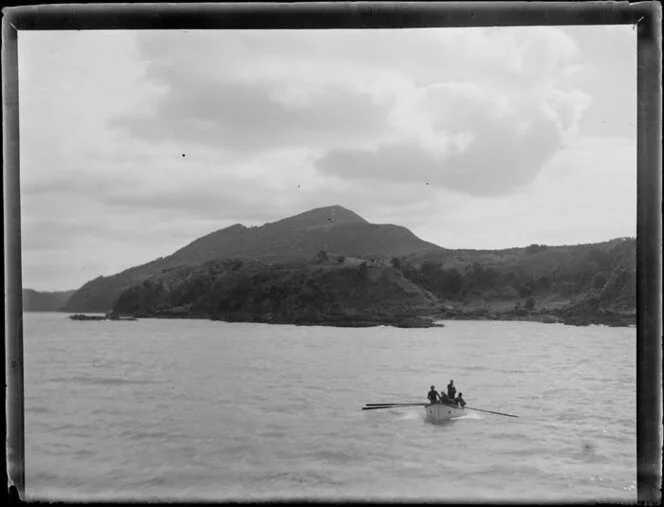 Group of four in a small rowing boat off an unidentified coastline