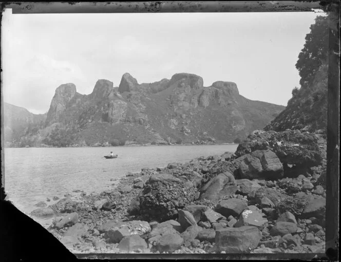 A man in a rowing boat in a channel betwenn two rocky outcrops, unidentified location