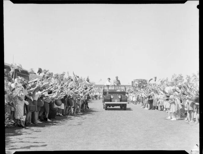 Queen Elizabeth II and the Duke of Edinburgh standing in the back of a Land Rover as it drives past a crowd of children at Athletic Park, Wellington, Royal Tour 1953-1954