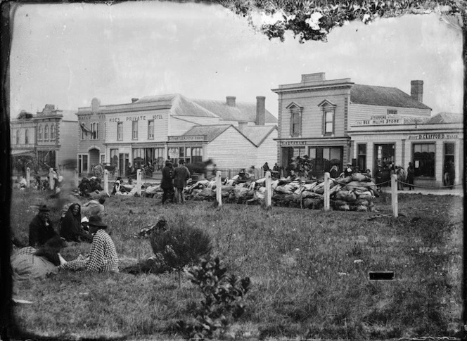Palmerston North street scene, with Maori group on grass in foreground