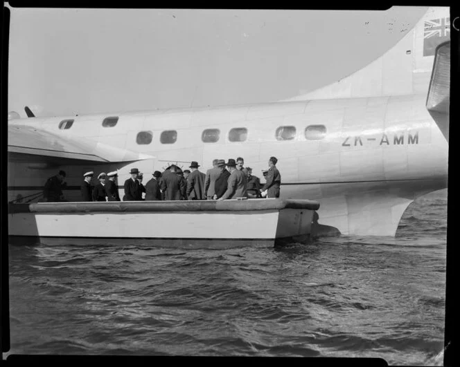 Unidentified passengers and Tasman Empire Airways Limited crew board the Short S.45 Solent flying boat, R.M.A Araragi (ZK-AMM), from a small boat drawn up alongside it, Evans Bay, Wellington
