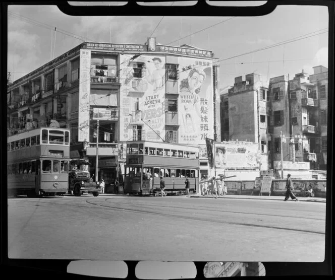 Street scene, Hong Kong, featuring double-decker trams and including advertisments for Levers Health Soap, White Rose [perfume? shampoo?], and the Roxy Theatre